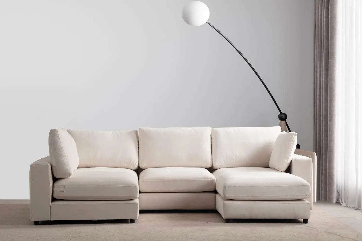 Canapé JULIA modulable en velours blanc cassé 4 places avec 1 pouf, présenté dans un intérieur minimaliste avec une lampe d'arc élégante et une lumière naturelle douce.