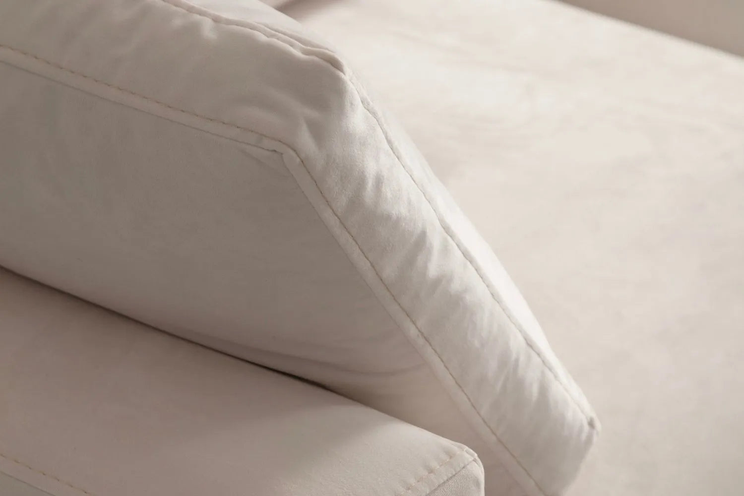 Gros plan sur l'angle d'un coussin du canapé JULIA modulable en velours blanc cassé, mettant en valeur la couture et la qualité du tissu.